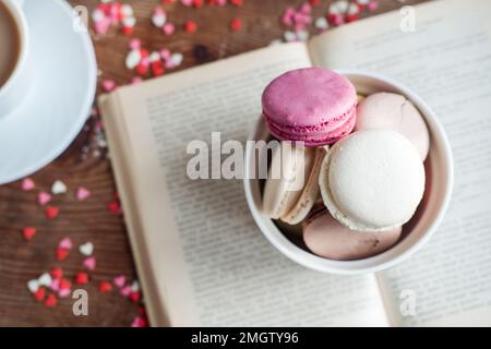 Macaroons in a bowl, a cup of coffee, on a background of small hearts on a wooden background Stock Photo