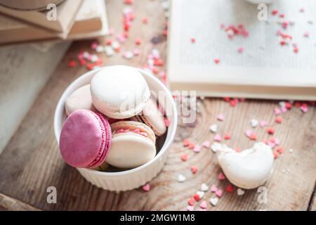 Macaroons in a bowl on a book background of small hearts on a wooden background,top view Stock Photo