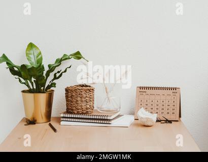 Living room interior with wooden table, white flowers in vase, houseplant, calendar and accessories in modern home decor. Copy space. Front view Stock Photo