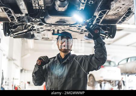 Professional car mechanic under a car on a lift using an LED lamp and repair tools. High-quality photo Stock Photo
