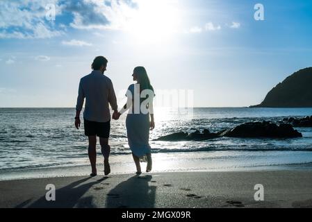 silhouette of young engaged couple holding hands in love during the sunset on a sandy island beach Stock Photo