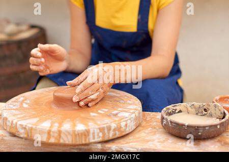 woman potter in yellow T-shirt and blue apron makes product out of clay Stock Photo