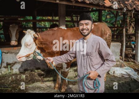 a moslem man with skullcap standing holding the cow's bridle Stock Photo