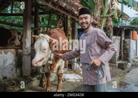 a moslem man with skullcap standing and holding the cow's bridle Stock Photo