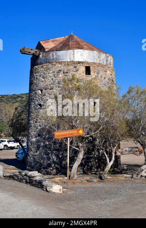 Elounda, Crete,Greece - October 10, 2022: Old windmills built of stone in Elounda on Kalydon peninsula with signs to tavern and old church Stock Photo