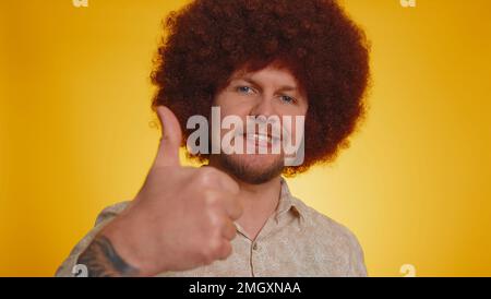 Great job, nice. Cheerful positive happy bearded man with afro hairstyle showing thumbs up, nodding in approval, successful good work. Young stylish guy on yellow background. People sincere emotions Stock Photo