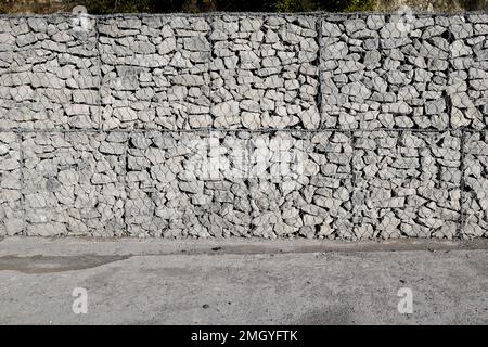 grey stone and pebbles in wire mesh wall horizontal stones facade background with grey floor cement Stock Photo