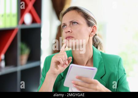 Thinking business woman making notes in her notebook while sitting in office. Stock Photo