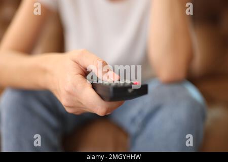 Woman holds remote control in her hand while sitting on sofa. Stock Photo