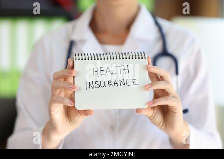 Female doctor shows notepad with words health insurance close up. Stock Photo