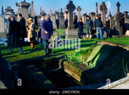 Man Throwing Handful of Earth On to Coffin after Funeral at Cemetery in Glasgow Scotland Stock Photo