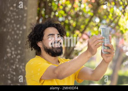portrait of a Mexican man smiling with afro and beard taking selfie Stock Photo