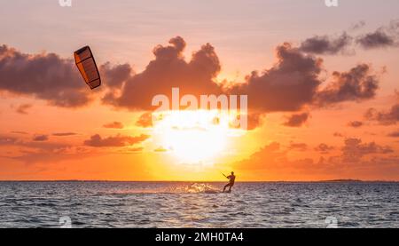 Sunset sky over the Indian Ocean bay with a kiteboarder riding kiteboard with a green bright power kite. Active sport people and beauty in Nature conc Stock Photo