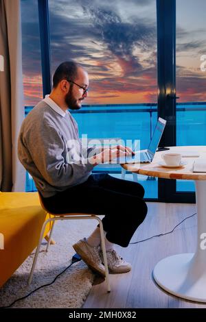 Man in eyeglasses working at laptop at home. Internet business, freelance or distance job concept. Stock Photo