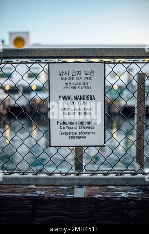 sign on Seattle waterfront, Pier 70, stating 'no fishing no generators at all times' in Korean, Filipino (Tagalog), and Russian Stock Photo