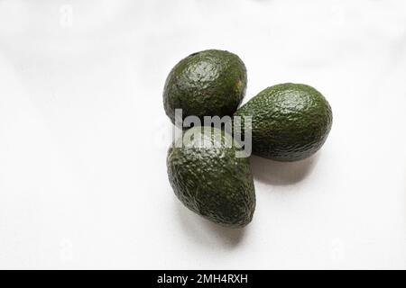 Three whole green avacados, Persea americana, ripening on a white countertop. Closeup, Stock Photo