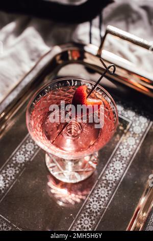 pink sparkling wine drink with strawberry heart garnish on silver tray on bed with black cat Stock Photo