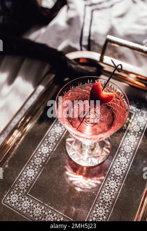 pink sparkling wine drink with strawberry heart garnish on silver tray on bed with black cat Stock Photo