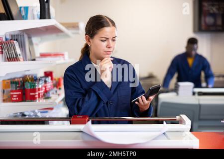 Female employee of printing house counts the cost of work on calculator Stock Photo