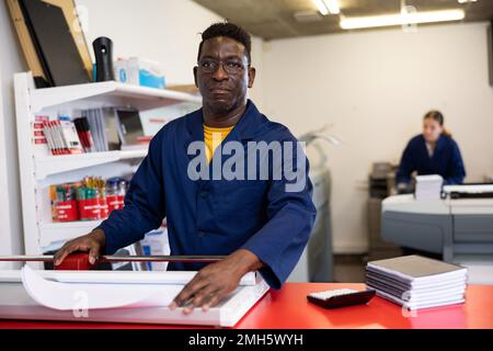 Serious print shop worker cuts paper on professional cutter Stock Photo
