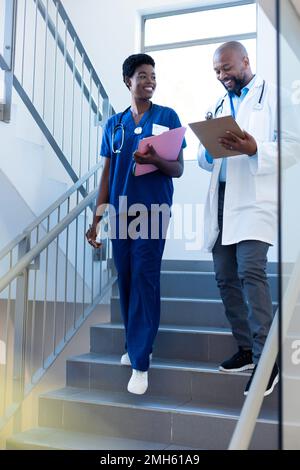 Vertical of happy african american female and male doctor talking on hospital staircase Stock Photo