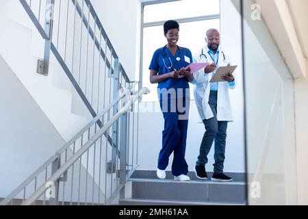 Happy african american female and male doctor talking on hospital staircase Stock Photo