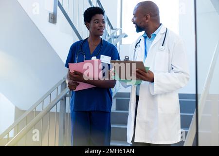 Happy african american female and male doctor talking on hospital staircase Stock Photo