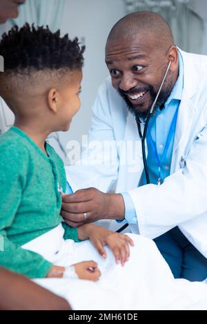 Smiling african american male doctor using stethoscope on boy patient Stock Photo