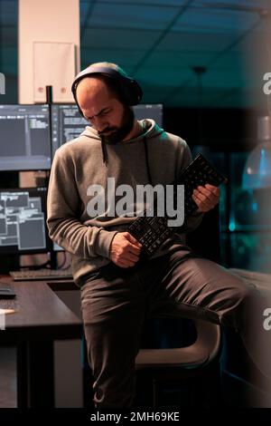 Young coder fooling around with keyboard playing guitar, working on user interface with multiple screens parsing algorithm in software agency. Writing code and programming server. Stock Photo