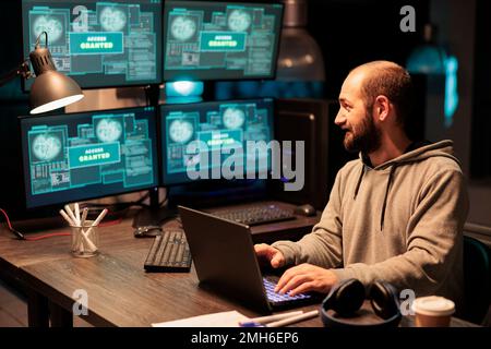 Young hacker stealing programming data from server, wearing hoodie and doing cyberterrorism with multiple screens. Server hacking and cyberattacks using virus to infect IT system. Stock Photo