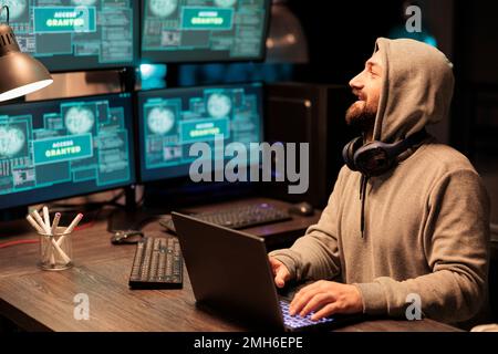 IT male hacker using computer to break system firewall, hacking security server. Dangerous thief breaking database and stealing information, working late at night with multiple monitors. Stock Photo