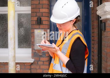 Close-up photo of a female civil engineer inspecting a building construction site and taking notes on her notepad, hard hat and orange high vis vest Stock Photo