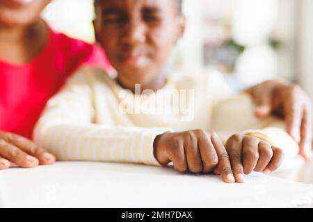 Happy african american grandmother and blind granddaughter reading braille Stock Photo