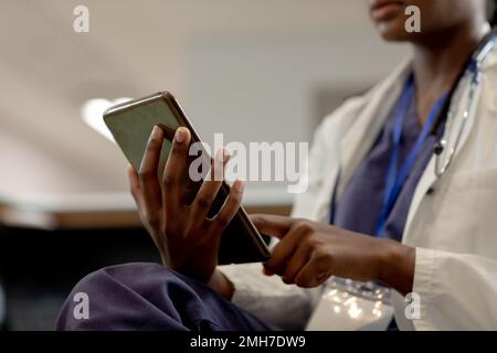 African american female doctor working at hospital, using smartphone Stock Photo