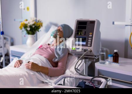 Senior caucasian female cancer patient wearing head scarf in bed with oxygen mask at hospital Stock Photo