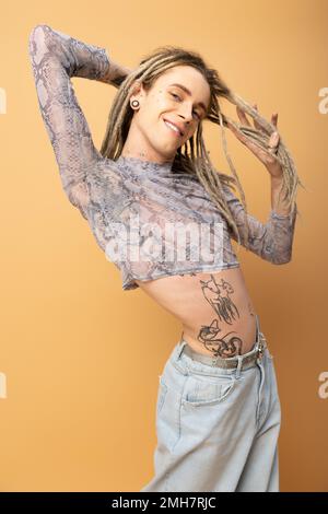 Smiling queer person touching dreadlocks and looking at camera isolated on yellow,stock image Stock Photo