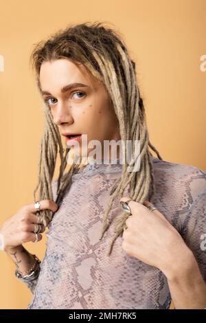 Nonbinary person touching dreadlocks and looking at camera isolated on yellow,stock image Stock Photo