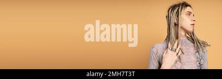 Young queer person touching dreadlocks and looking away isolated on yellow, banner,stock image Stock Photo