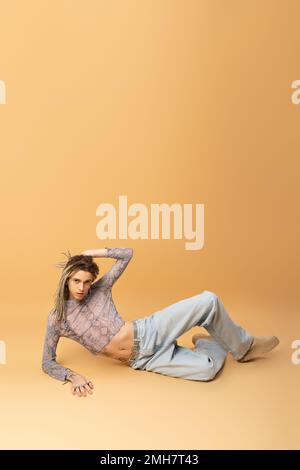 Trendy nonbinary person touching dreadlocks and looking at camera on yellow background,stock image Stock Photo
