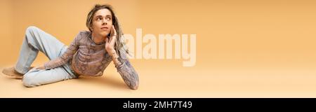 Young queer person in top and jeans lying on yellow background, banner,stock image Stock Photo