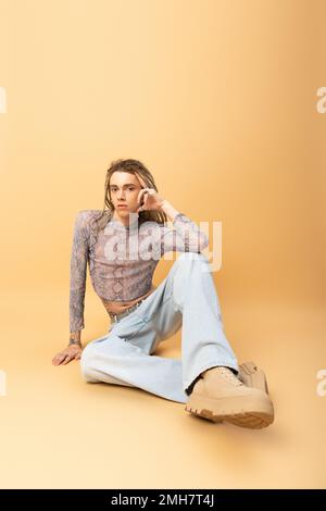 Full length of nonbinary person looking at camera while sitting on yellow background,stock image Stock Photo