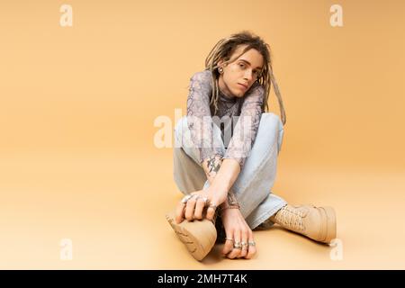 Young tattooed queer person posing on yellow background,stock image Stock Photo