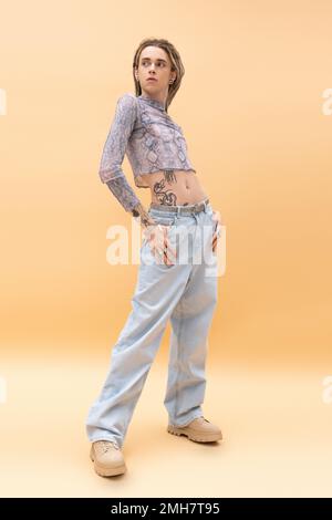 Full length of trendy nonbinary person posing in crop top and jeans on yellow background,stock image Stock Photo