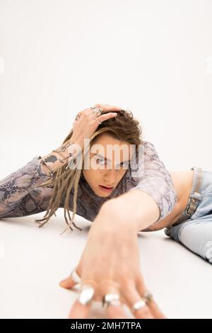 Tattooed nonbinary person looking at camera while lying on white background,stock image Stock Photo
