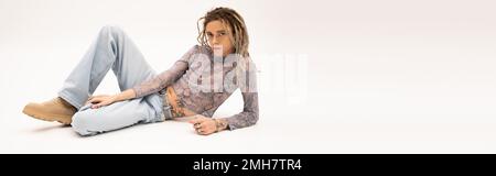 Queer person with dreadlocks looking at camera while lying on white background, banner,stock image Stock Photo