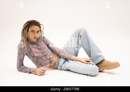 Tattooed nonbinary person in crop top with snakeskin print and jeans lying on white background,stock image Stock Photo