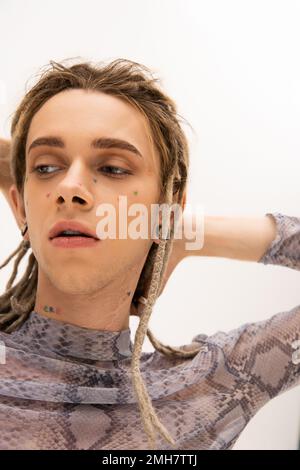 Portrait of tattooed queer person touching dreadlocks and looking away isolated on white,stock image Stock Photo