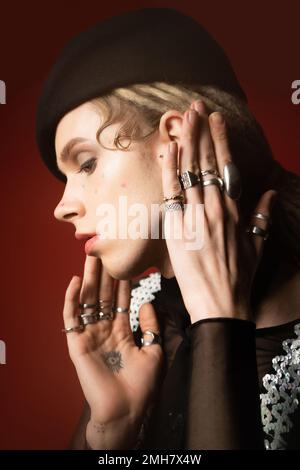 portrait of tattooed nonbinary model in silver rings and black beret on dark red,stock image Stock Photo
