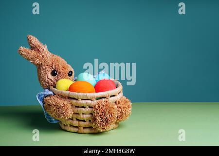 Easter colorful eggs in a straw bunny basket on green blue background. Happy Easter. Stock Photo