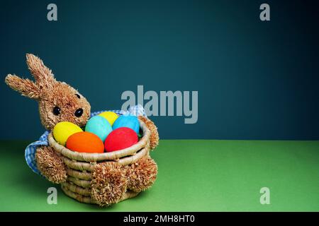 Easter colorful eggs in a straw bunny basket on green blue background. Happy Easter. Stock Photo